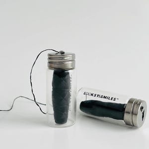 May include: Two glass jars with black dental floss inside. The jars have silver lids and are labeled "LOOKSYISMILES".