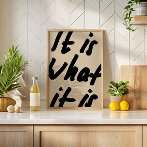 It Is What It Is poster in beige and black with a handwritten quote design. Modern wall art for calm, chill vibes and effortless style. Perfect for living room, office, or bedroom decor.