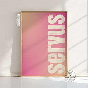 May include: A framed art print with a gradient background of pink and peach hues. The word "SERVUS" is printed vertically in a bold, off-white font. The frame is gold, and the text "ALL COLORS AVAILABLE" is printed on the left side.