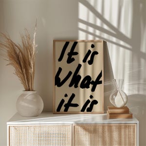 It Is What It Is poster in beige and black with a handwritten quote design. Modern wall art for calm, chill vibes and effortless style. Perfect for living room, office, or bedroom decor.