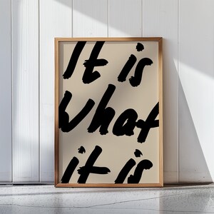 It Is What It Is poster in beige and black with a handwritten quote design. Modern wall art for calm, chill vibes and effortless style. Perfect for living room, office, or bedroom decor.