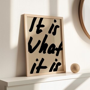 It Is What It Is poster in beige and black with a handwritten quote design. Modern wall art for calm, chill vibes and effortless style. Perfect for living room, office, or bedroom decor.