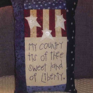 May include: A handmade pillow with a patriotic theme. The pillow is made of blue, red, and white fabric and features a stitched design of stars and stripes. The pillow has a white fabric panel with the words "My country tis of thee sweet land of liberty" stitched in black thread.