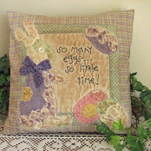 May include: A decorative pillow with a patchwork design featuring a bunny, eggs, and the text "So many eggs, so little time!" The pillow is made of a variety of fabrics in shades of brown, green, purple, and pink.