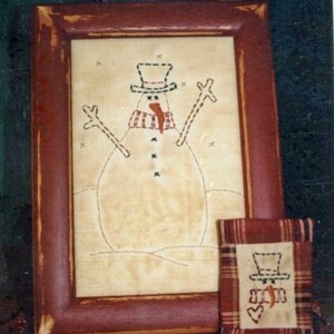 May include: A framed cross-stitch of a snowman with a red scarf and black buttons. The frame is a distressed red wood with a smaller framed cross-stitch of a snowman with a red heart on a plaid background.