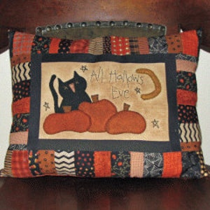 May include: A black and orange patchwork pillow with a black cat, pumpkins, and a crescent moon. The pillow has the text "All Hallows Eve" embroidered on it.