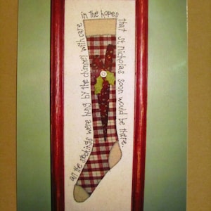 May include: A framed cross-stitch piece depicting a red and white plaid stocking with a green holly sprig and the text "in the hopes that St. Nicholas soon would be there... all the stockings were hung by the chimney with care."
