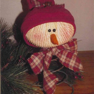 May include: A snowman made from a white, textured material with a red hat and a plaid bow. The snowman is sitting on a metal spring.