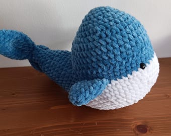May include: A blue and white crocheted whale plush toy. The whale has a white belly and a blue body with a textured surface.