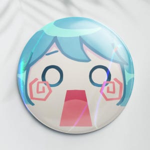 May include: A round, holographic button featuring a surprised cartoon character with blue hair and large eyes. The character's mouth is open, and pink swirls accent the cheeks. The button has a glossy finish and a white background.