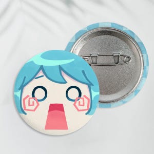 May include: Two round pinback buttons. One button features a cartoon face with blue hair, large black eyes, and a surprised expression. The other button shows the pinback mechanism. The background of the pin is light blue and white.