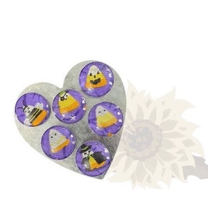 Puede incluir: Una bandeja de plata en forma de corazón con seis imanes redondos de color morado y blanco con diseños de maíz dulce y fantasmas con temática de Halloween.