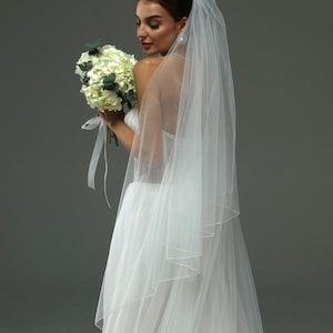 May include: A bride wearing a white wedding dress and veil, holding a bouquet of white flowers.