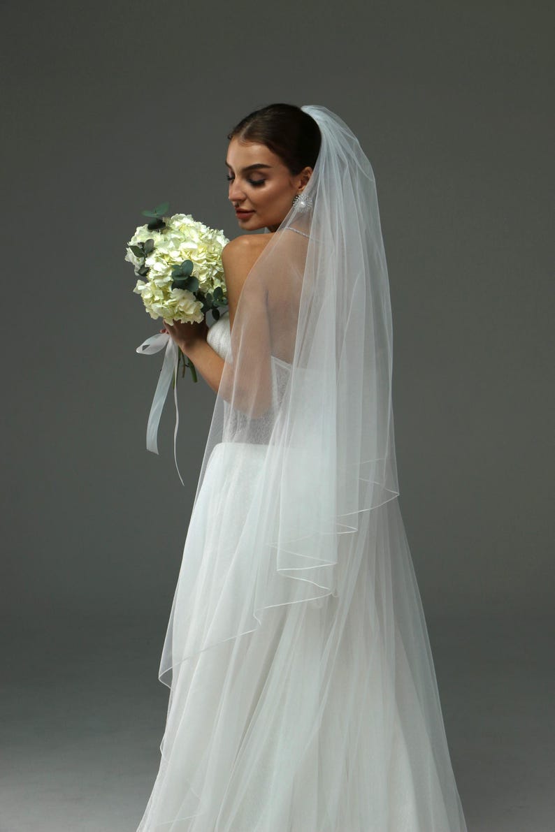 May include: A bride wearing a white wedding dress and veil, holding a bouquet of white flowers.
