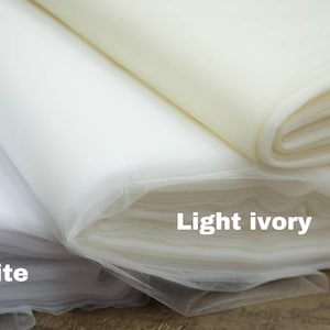 May include: Three rolls of tulle fabric in different shades of white: white, light ivory, and ivory.