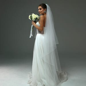 May include: A bride wearing a white wedding dress with a long veil and holding a bouquet of white flowers.