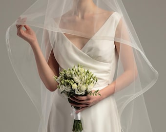 May include: A bride wearing a white wedding dress and a white veil holds a bouquet of white flowers.