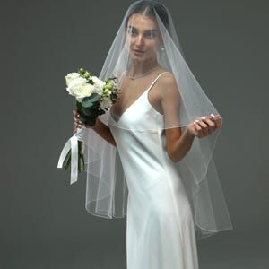 May include: A bride wearing a white wedding dress and veil, holding a bouquet of white flowers.