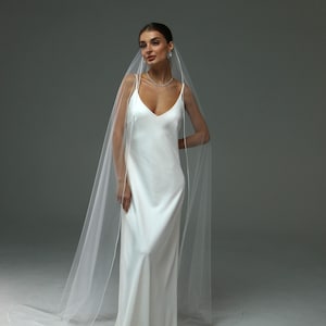 May include: A bride wearing a white satin wedding dress with a long, flowing veil. The veil is edged with a delicate white trim.
