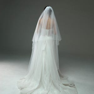 May include: A white wedding dress with a long veil. The dress has a fitted bodice and a flowing skirt.