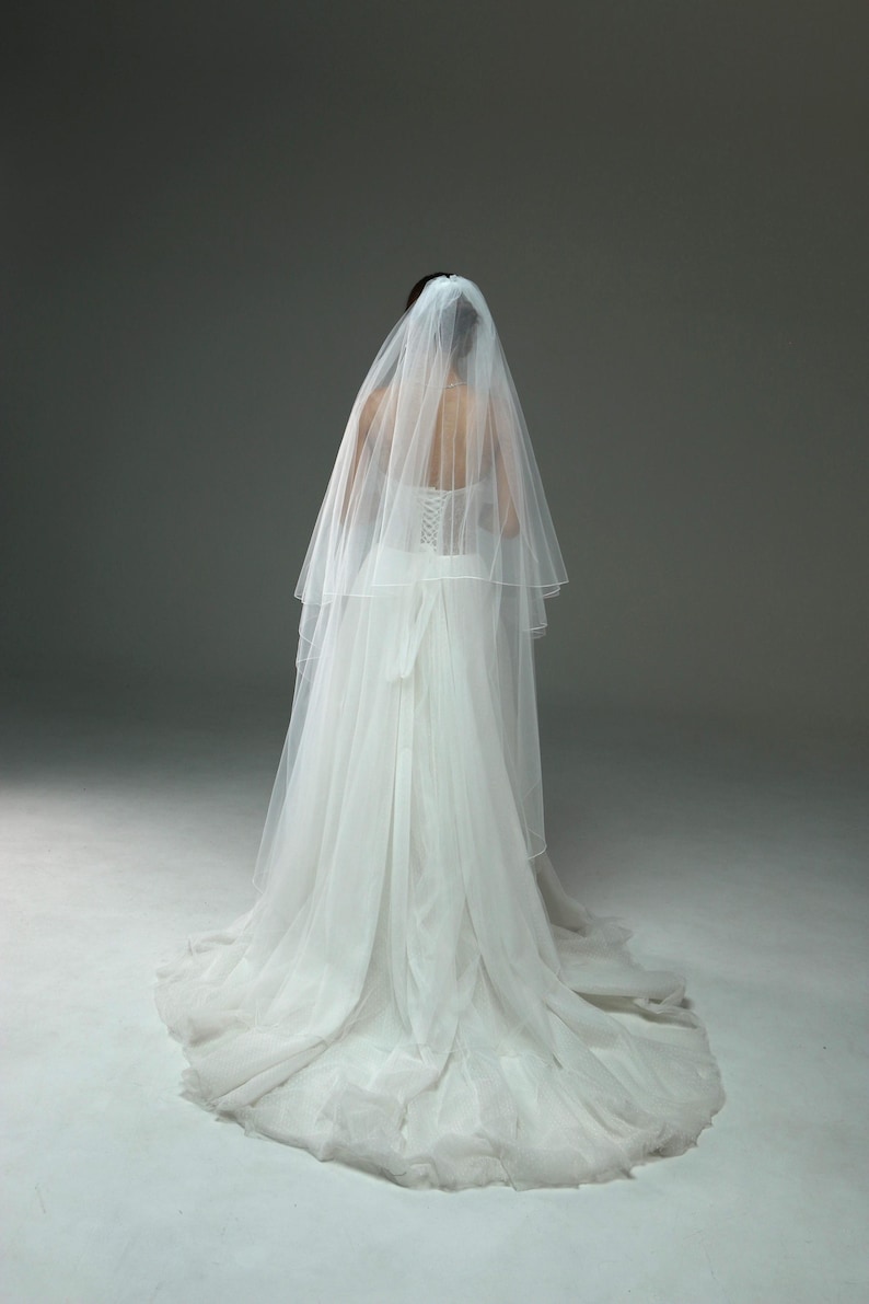 May include: A white wedding dress with a long veil. The dress has a fitted bodice and a flowing skirt.