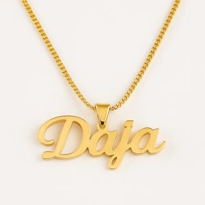 May include: A gold necklace featuring a cursive pendant spelling "Daja". The pendant hangs from a matching gold chain. The necklace is set against a plain white backdrop.