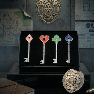Op de afbeelding: Een set van vier decoratieve sleutels met speelsymbolen: een roze ruit, een rood hart, een groene klaver en een blauwe schoppen. De sleutels worden gepresenteerd in een zwarte doos, met een Raccoon Police Department-badge op de achtergrond.