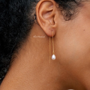 Könnte beinhalten: Ein Paar goldene Kettenohrringe mit jeweils einer einzelnen weißen Perle, die an der Kette baumelt.