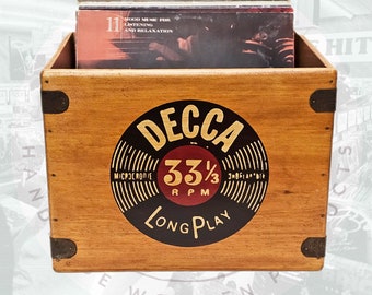 Może przedstawiać: Drewniana skrzynia na płyty winylowe z czarną i białą etykietą Decca 33 1/3 RPM Long Play. Skrzynia jest brązowa i ma metalowe akcenty. Skrzynia jest wypełniona płytami winylowymi.