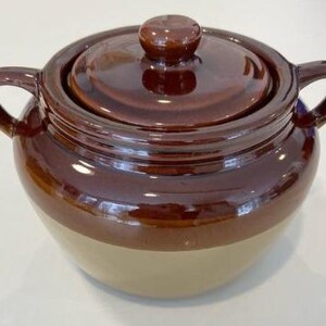 Peut inclure: Un pot en céramique bicolore avec un couvercle. Le pot est de couleur marron foncé sur la moitié supérieure et de couleur beige sur la moitié inférieure. Il a deux poignées et un bouton sur le couvercle. Le pot est probablement utilisé pour la cuisine ou le stockage.