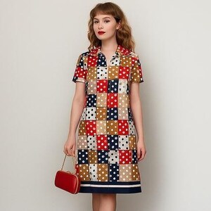 Peut inclure: Robe vintage à motif patchwork avec des carrés rouges, blancs, marine et beiges à pois blancs. La robe a un col, des manches courtes et une fermeture éclair sur le devant. Un petit sac à main rouge avec une chaîne dorée est tenu.