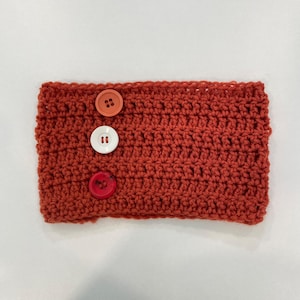 Peut inclure: Un cache-oreilles au crochet de couleur rouille avec trois boutons décoratifs orange, blanc et rouge. Cet accessoire fait à la main est conçu pour garder les oreilles au chaud et est un article d'hiver confortable.
