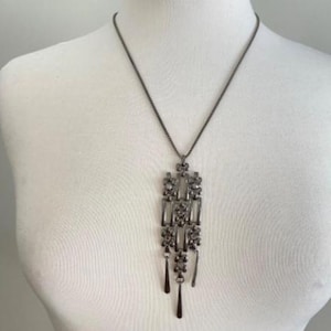Peut inclure: Un collier de couleur canon de fusil avec un pendentif rectangulaire orné d'éléments en forme de goutte. Le collier est présenté sur un mannequin blanc, mettant en valeur ses détails complexes et son style élégant.