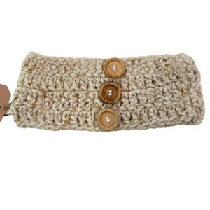 Peut inclure: Un bandeau beige crocheté avec trois boutons en bois. Le bandeau est fait d'un fil texturé avec des mouchetures marron et beige. Les boutons sont ronds et ont deux trous.