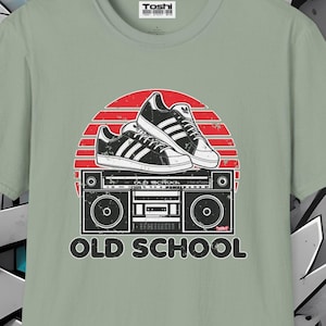 Könnte beinhalten: Ein salbeigrünes T-Shirt mit einer Retro-Grafik eines Boombox mit einem Paar Turnschuhen darauf. Die Grafik ist vor einem roten und orangefarbenen Sonnenuntergang platziert. Der Text "OLD SCHOOL" ist unter der Grafik gedruckt.
