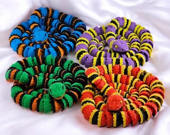 May include: Four colorful rubber snake toys, each with black and white stripes. The snakes are coiled up and have different colored bodies: blue, purple, green, and orange.