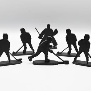 Puede incluir: Un conjunto de seis figuras de jugadores de hockey negros. Las figuras están todas en diferentes poses, algunas sosteniendo palos de hockey y otras sosteniendo discos. Las figuras están hechas de un material plástico duradero y son perfectas para cualquier aficionado al hockey.