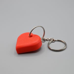 Op de afbeelding: Een rode hartvormige sleutelhanger met een zilveren metalen ring en ketting.