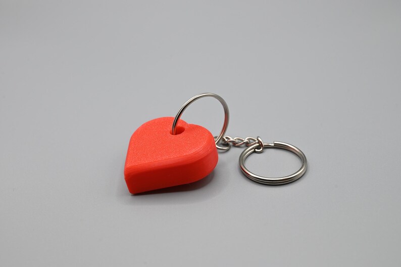 Op de afbeelding: Een rode hartvormige sleutelhanger met een zilveren metalen ring en ketting.