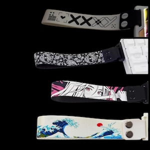 May include: Four fabric wrist straps attached to mechanical keyboard components. The top strap is beige with black geometric symbols. The second is black with a white paisley pattern. The third features a pink and black anime character. The bottom is white with a blue wave graphic.