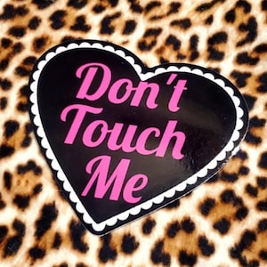 May include: A black heart-shaped sticker with a white scalloped border. The sticker says "Don't Touch Me" in pink letters.