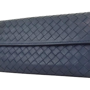 Puede incluir: Una cartera de cuero tejido azul oscuro con cierre de solapa.