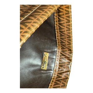 May include: A brown leather handbag with a gold metal logo that reads "Anne Klein." The bag has a brown and gold patterned fabric lining.
