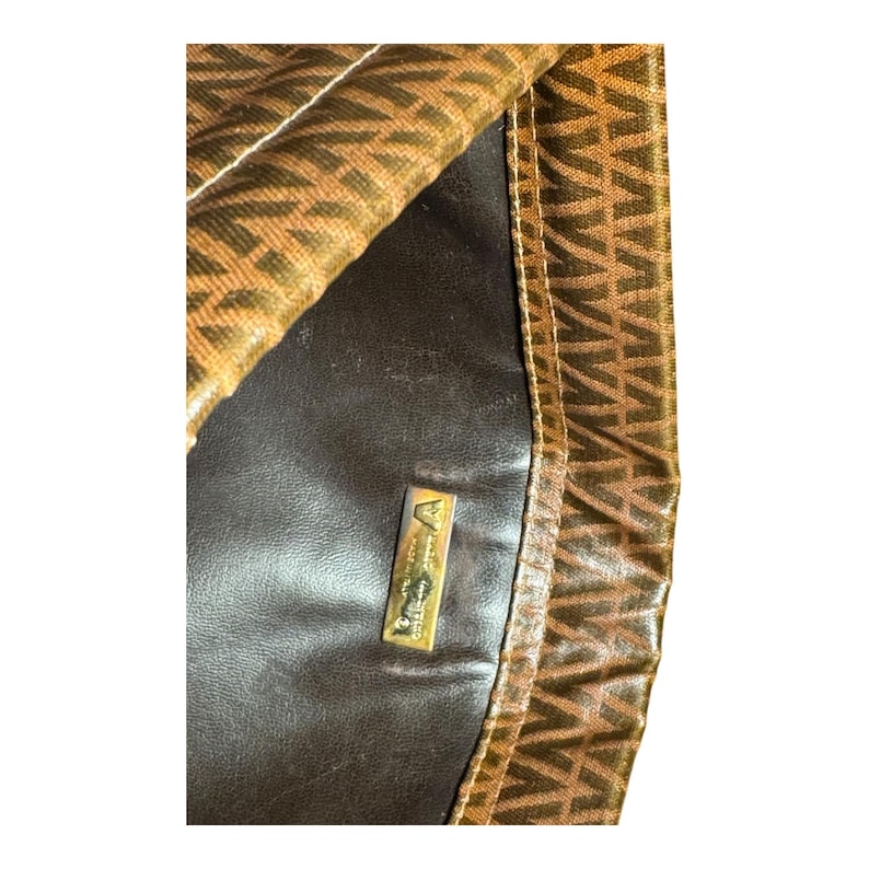 May include: A brown leather handbag with a gold metal logo that reads "Anne Klein." The bag has a brown and gold patterned fabric lining.