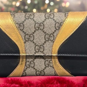May include: A black and beige wallet with gold accents. The wallet has a GG pattern and a curved design.