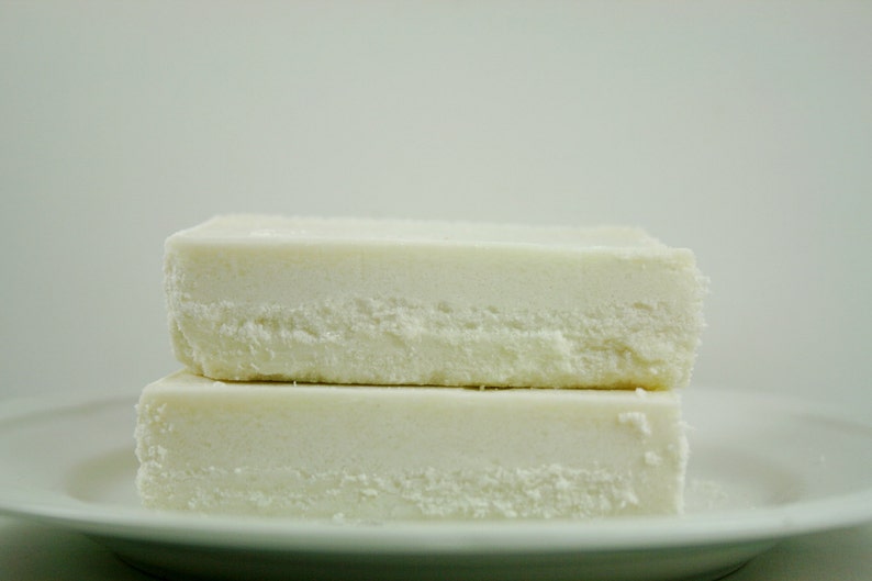 May include: Two white blocks of tofu stacked on a white plate. The tofu is soft and creamy, with a slightly grainy texture.
