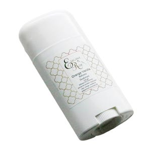 Op de afbeelding: Witte deodorantstick met een etiket met de tekst "Elegant & R Orange Vanilla Botanical Deodorant". Het etiket heeft een gouden vierpasontwerp. De deodorant is 128 gram.