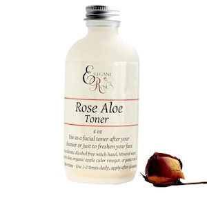 Puede incluir: Una botella de vidrio transparente con una tapa plateada, etiquetada como "Rose Aloe Toner" y "4 oz". La botella está sobre una superficie blanca con un capullo de rosa seco al lado. La etiqueta también incluye el texto "Usar como tónico facial después de su limpiador o simplemente para refrescar su rostro. Ingredientes: Hamamelis sin alcohol, agua mineral, aloe vera, vinagre de sidra de manzana orgánico, agua de rosas orgánica. Instrucciones: Usar 1-2 veces al día, aplicar después de la limpieza."