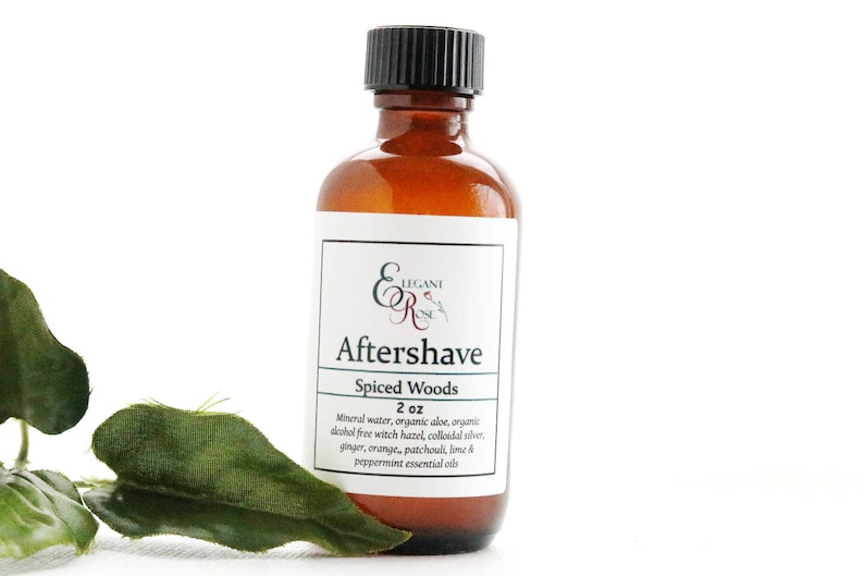 May include: A brown glass bottle of "Aftershave Spiced Woods" with a black cap and a white label. The label includes the brand name "Elegant R" and the product's ingredients. The bottle is 2 oz. and is next to a green leaf.