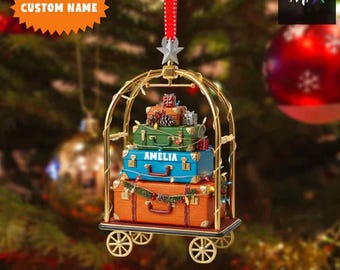 May include: A Christmas ornament shaped like a luggage cart, featuring a stack of colorful suitcases. The blue suitcase is labeled "AMELIA". The ornament is suspended by a red and white polka-dot ribbon. The text "CUSTOM NAME" and "2D FLAT ITEM" are also visible.